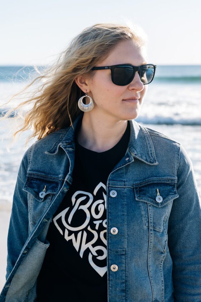 Woman in denim jacket and sunglasses enjoying a sunny beach day.