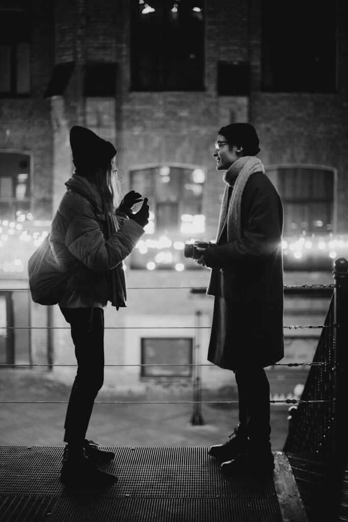 Stylish young couple in an urban street setting, engaging in a warm winter conversation at night.