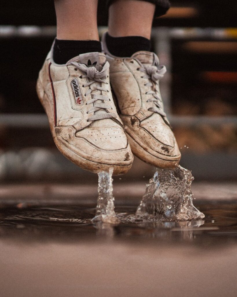 Worn white sneakers making a splash in a puddle, capturing a dynamic moment outdoors.
