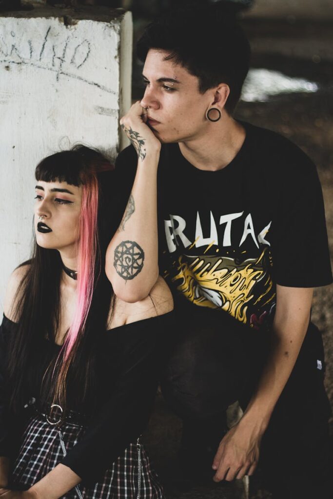Portrait of a young couple in goth attire, showcasing unique tattoos and piercings.