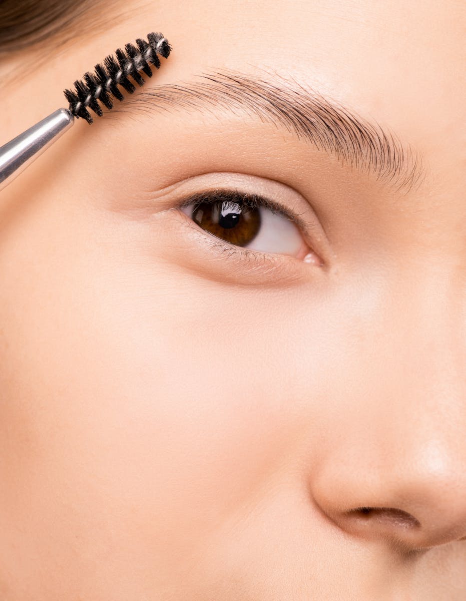 Detailed shot of a woman applying makeup to eyebrows using a brush, showcasing skincare routine.