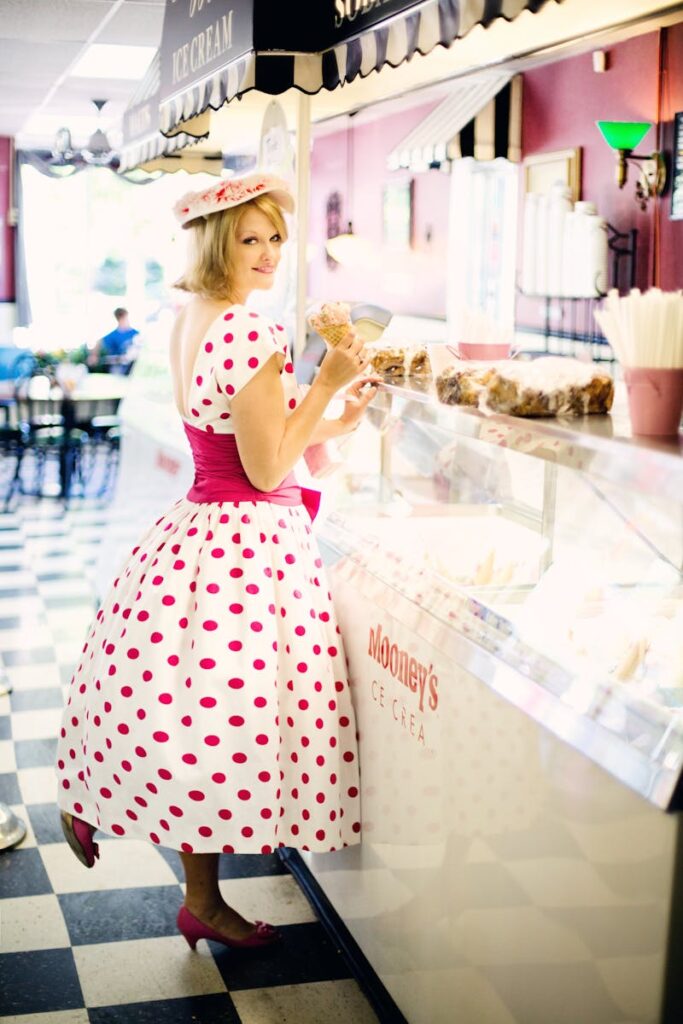 Woman in a vintage polka dot dress enjoying ice cream at a retro café.
