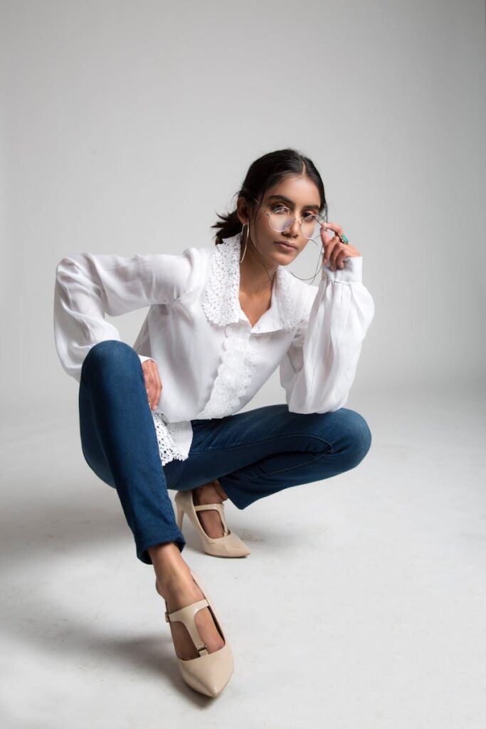 Stylish young woman in a white blouse and jeans posing indoors with a confident expression.