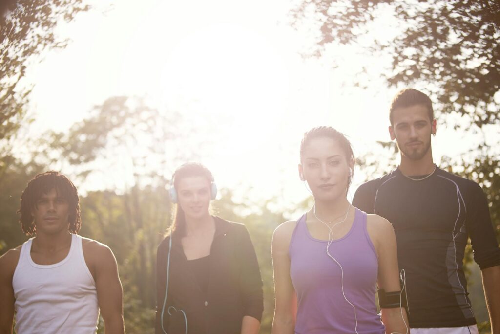 A group of young adults jogging outdoors with headphones and enjoying the sunny day.
