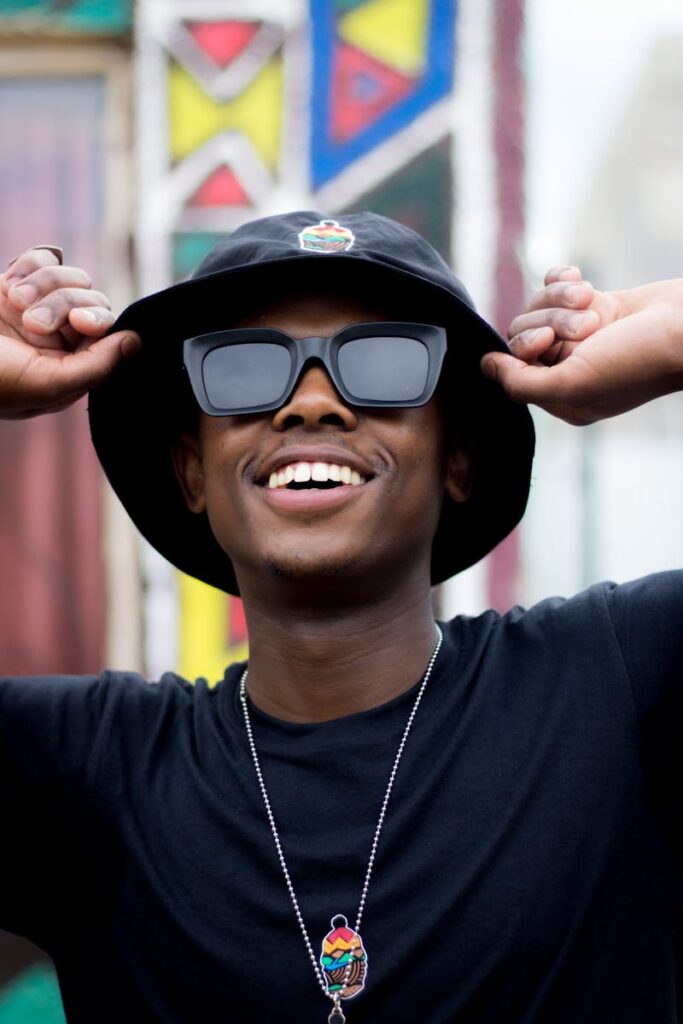 Confident young man smiling outdoors, wearing sunglasses and a stylish bucket hat.