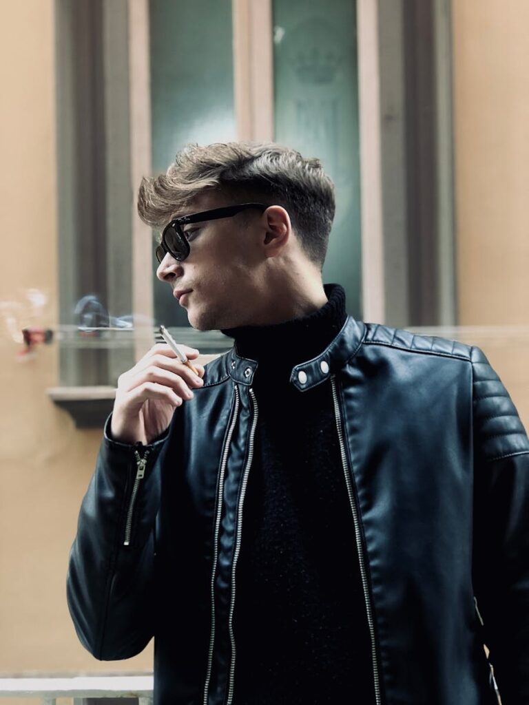 Fashionable man in black leather jacket and sunglasses smoking outdoors in Napoli.