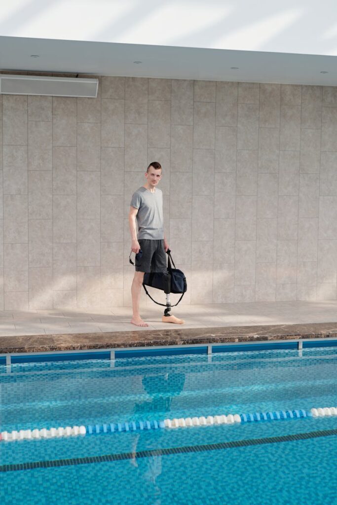 A man with a prosthetic leg stands confidently by an indoor swimming pool, ready for a workout.