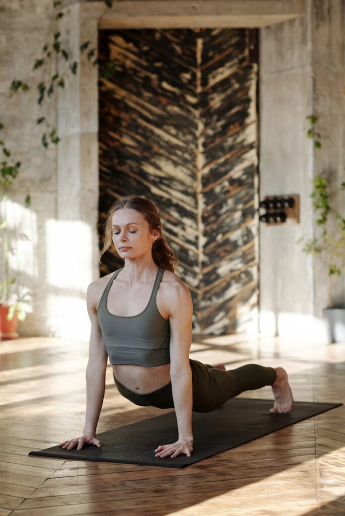 A woman practicing yoga, focusing on stretch and serenity in a sunlit room with natural decor.