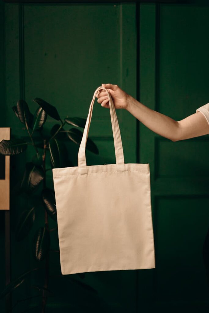 Simple cotton tote bag held by a hand against a green background, ideal for eco themes.