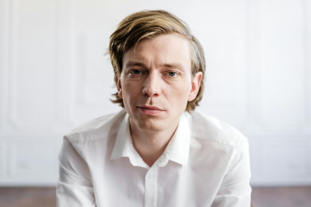 Close-up portrait of a man indoors in a bright white shirt, thoughtful expression.