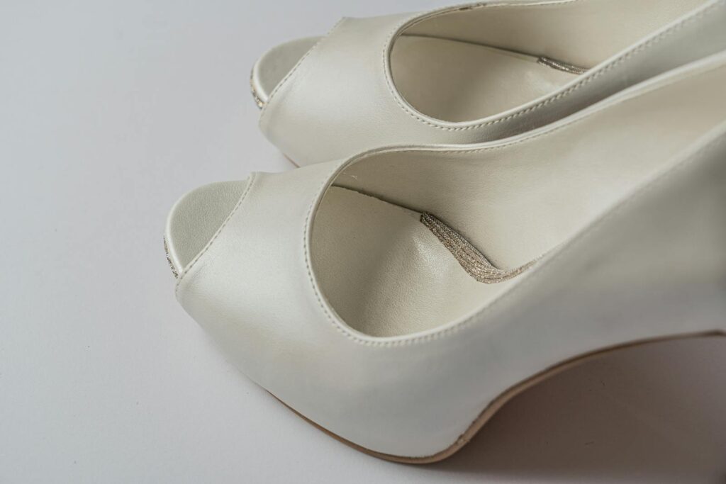 Close-up of elegant white peep-toe high heels on a neutral background.