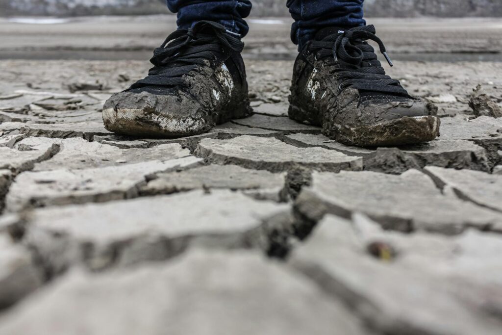 Close-up of muddy sneakers on cracked dry ground, symbolizing drought and resilience.