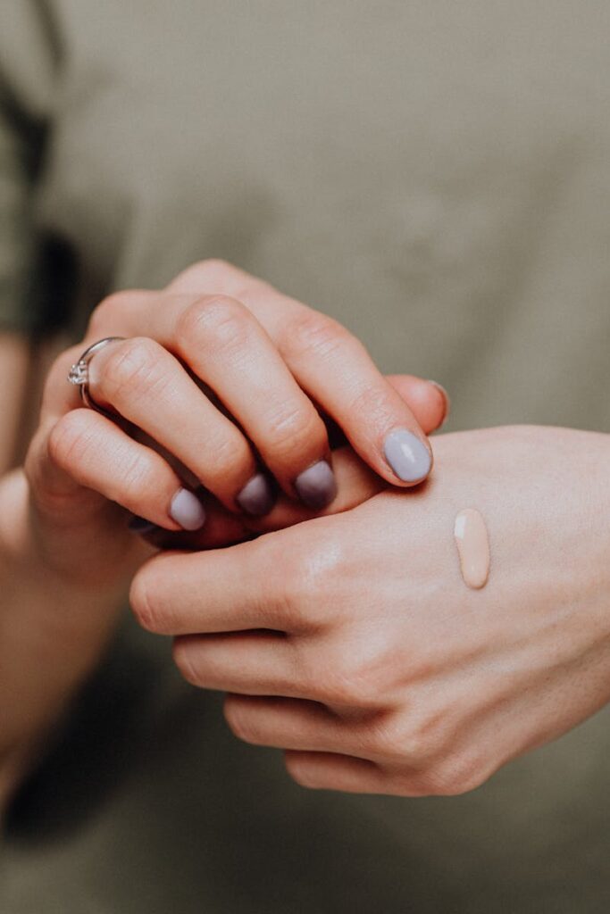 Crop unrecognizable female in casual clothes with manicured hands demonstrating drop of makeup foundartion on back of hand