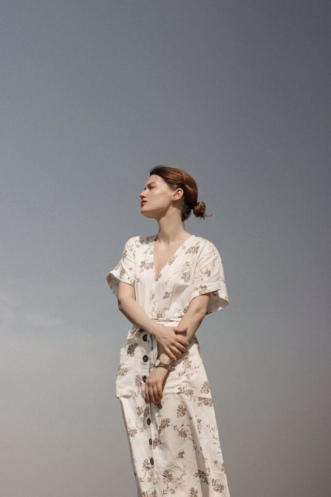 Portrait of a contemplative woman in a floral dress against a clear sky, exuding serenity and style.