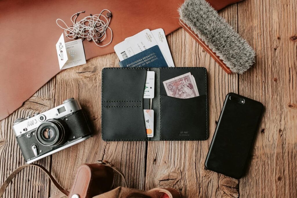 Flat lay of traveler essentials including wallet, camera, and phone on wooden surface.