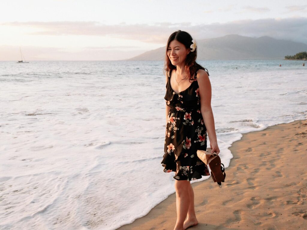 A young woman strolls along a serene seaside as the sun sets, embracing tranquility.