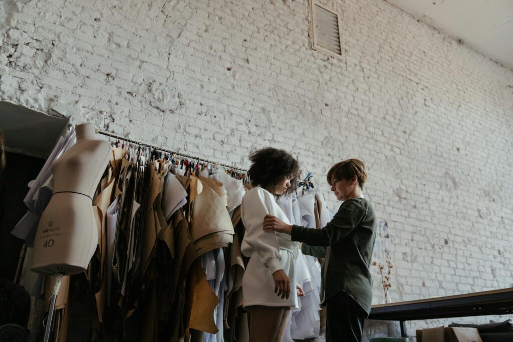 A fashion designer adjusts clothing on a model in a stylish atelier, showcasing creativity.