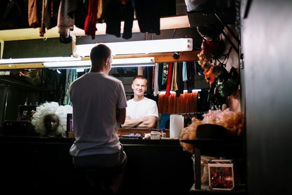 Man preparing backstage in a dressing room, focused on reflection in the mirror.