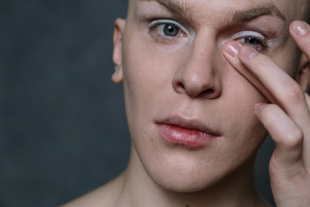 Portrait of a man applying makeup to his eyelid, showcasing a beauty routine.