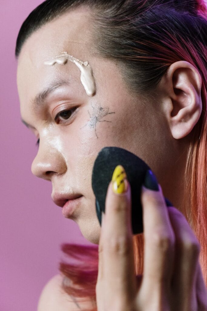 Young adult using makeup sponge with a bug detail on the face and colorful hair.