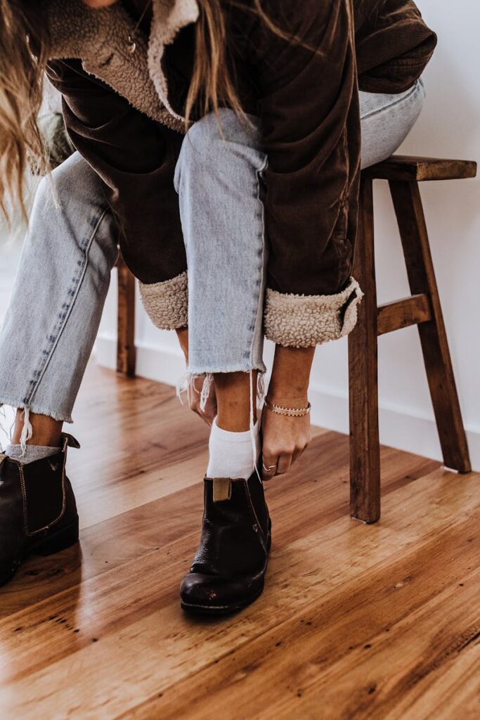 Woman in casual jeans and boots sitting indoors, showcasing a cozy fall style.