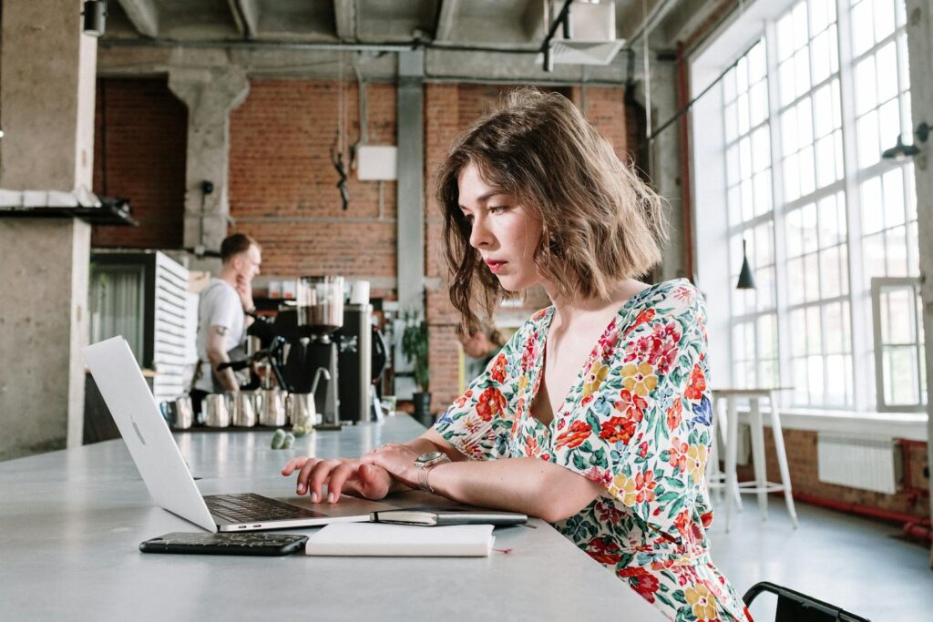 Focused young woman in floral dress using laptop in stylish cafe setting.