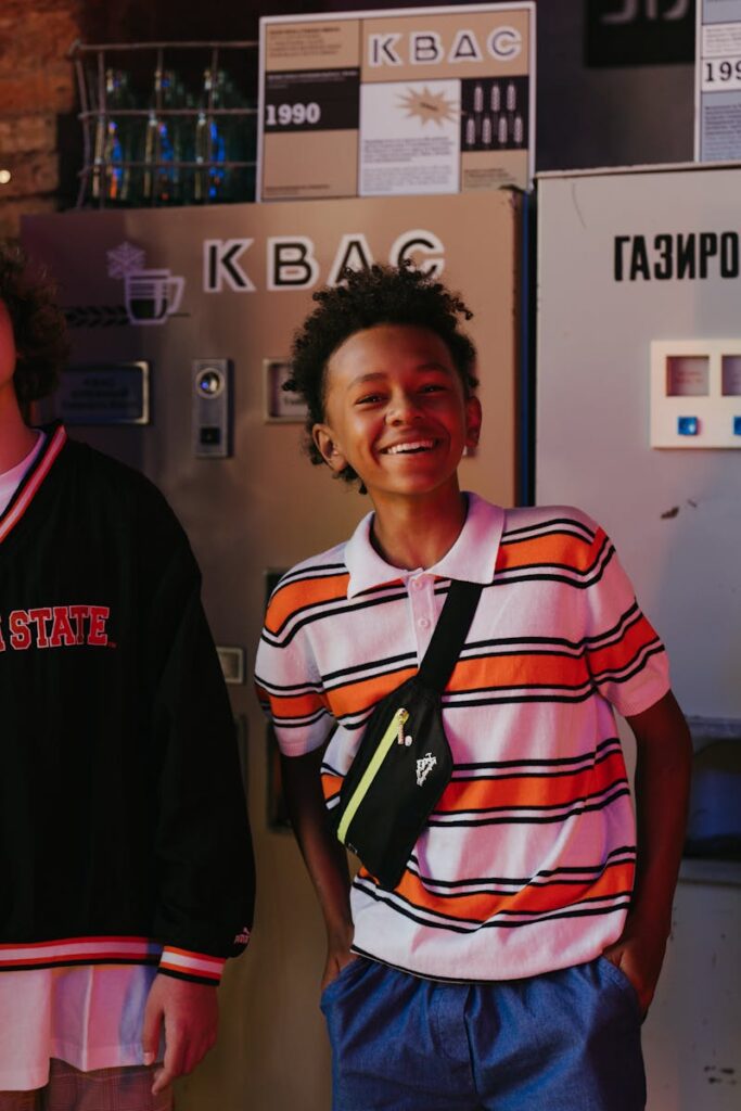 A joyful teen stands indoors in front of vintage vending machines, beaming with happiness.