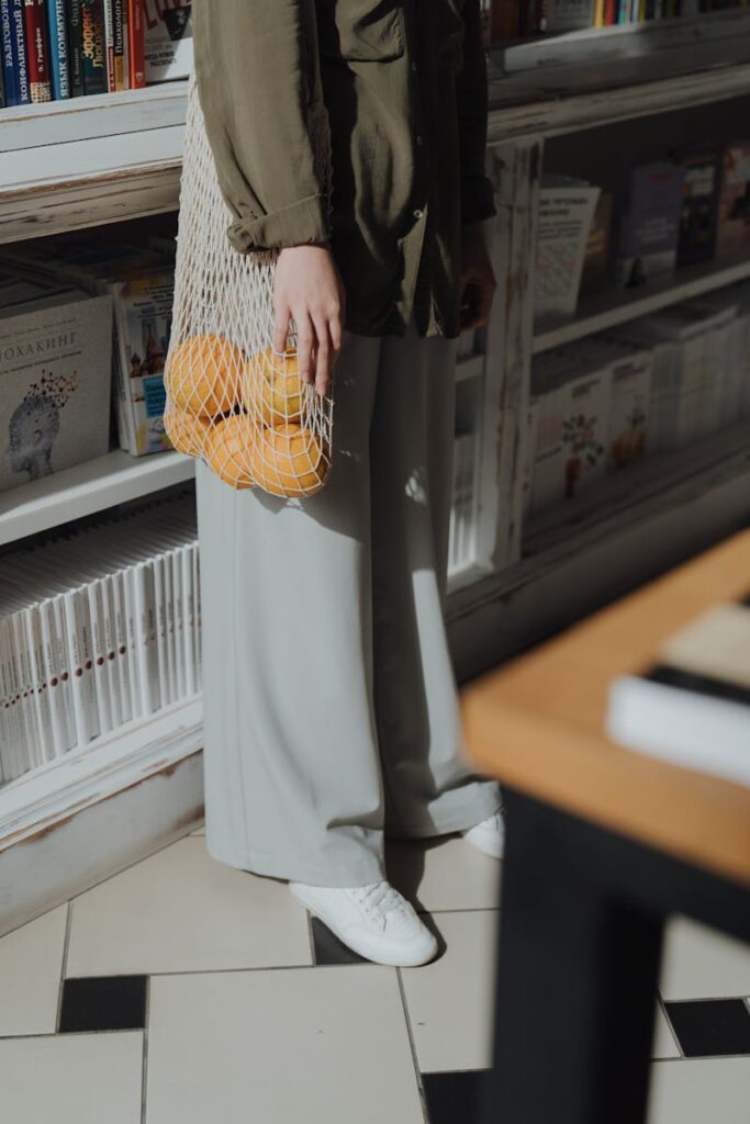 Woman holding eco-friendly string bag with oranges in a bookstore. Casual and sustainable shopping concept.