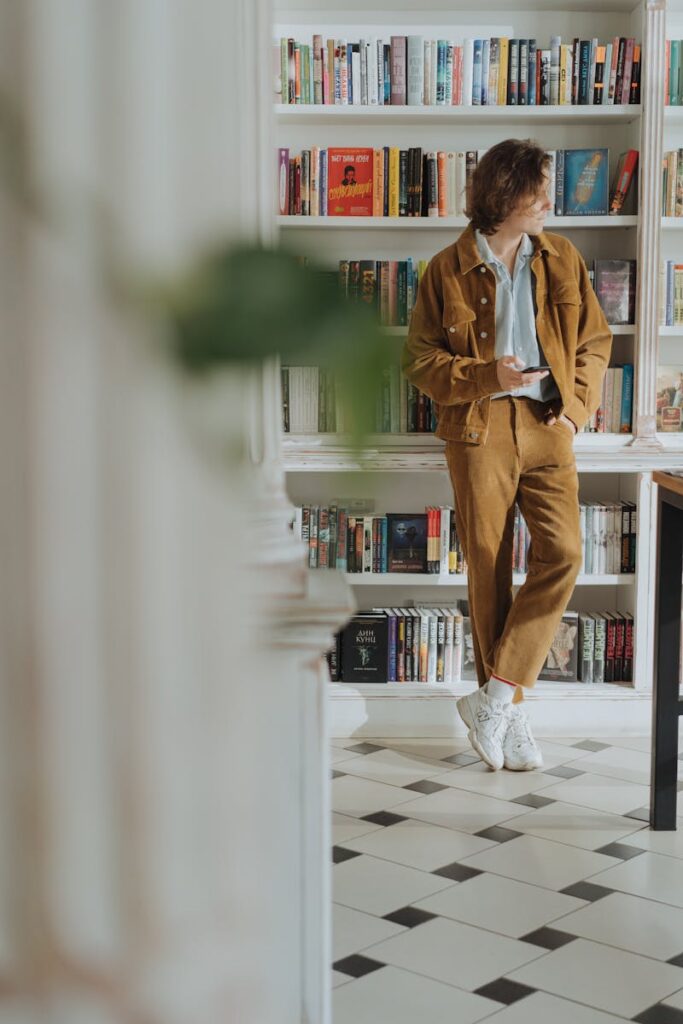 A young adult in a brown suit browsing books in a modern bookstore interior.