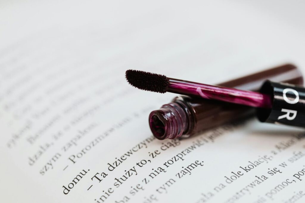 A vibrant lip gloss tube lies open on the pages of a book, adding a splash of color.