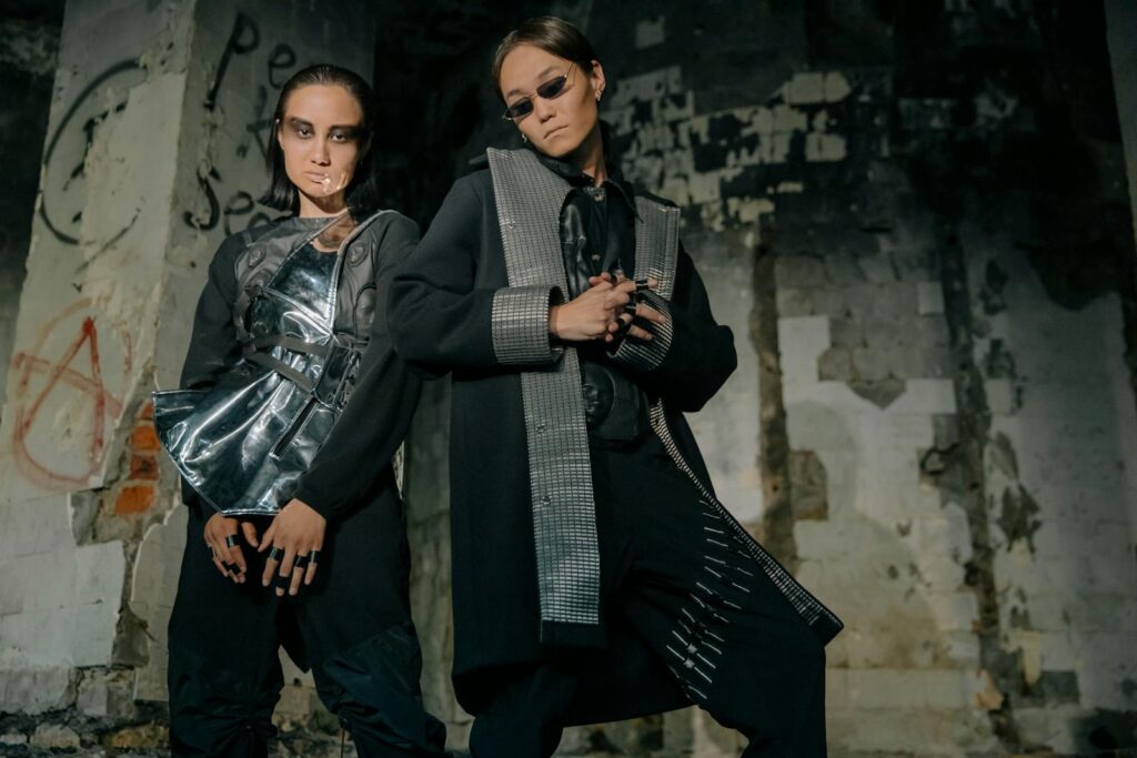 Two models pose in futuristic outfits against a dystopian urban backdrop.