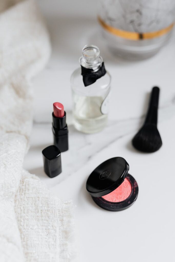 A flat lay of beauty products including lipstick, blush, and a perfume bottle on a marble surface.