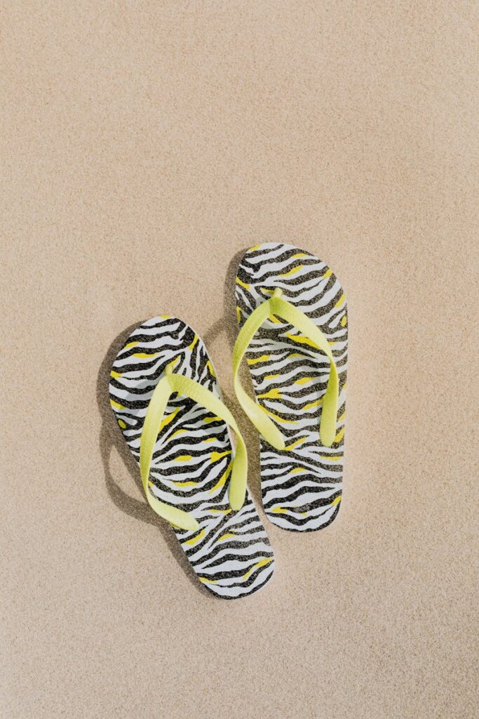 Stylish zebra print flip flops with yellow straps on a sandy beach surface.