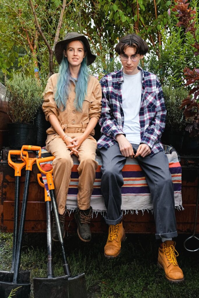 A teenage couple sitting on a wooden bench surrounded by plants and gardening tools.