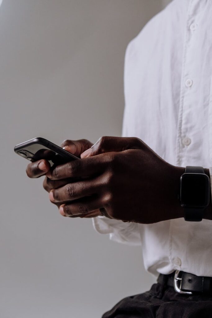 Close-up of a person in a white shirt using a smartphone and wearing a smartwatch, indoors.