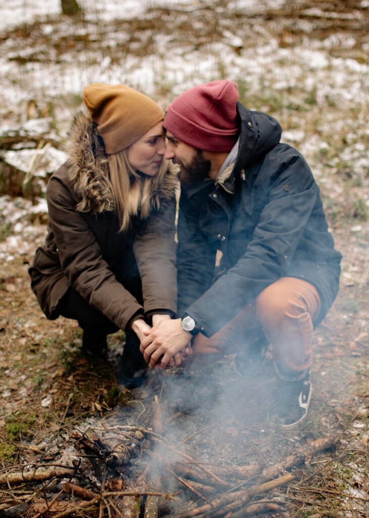 Happy couple holding hands by a bonfire in a fall setting, enjoying each other's company.