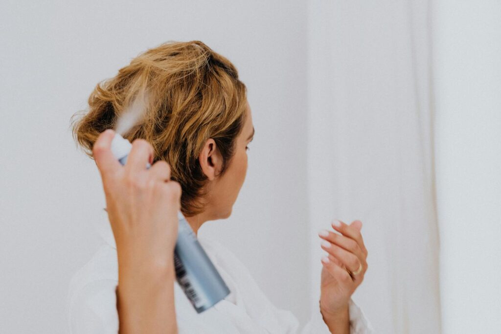 A woman uses hair spray for styling in a bright indoor setting.