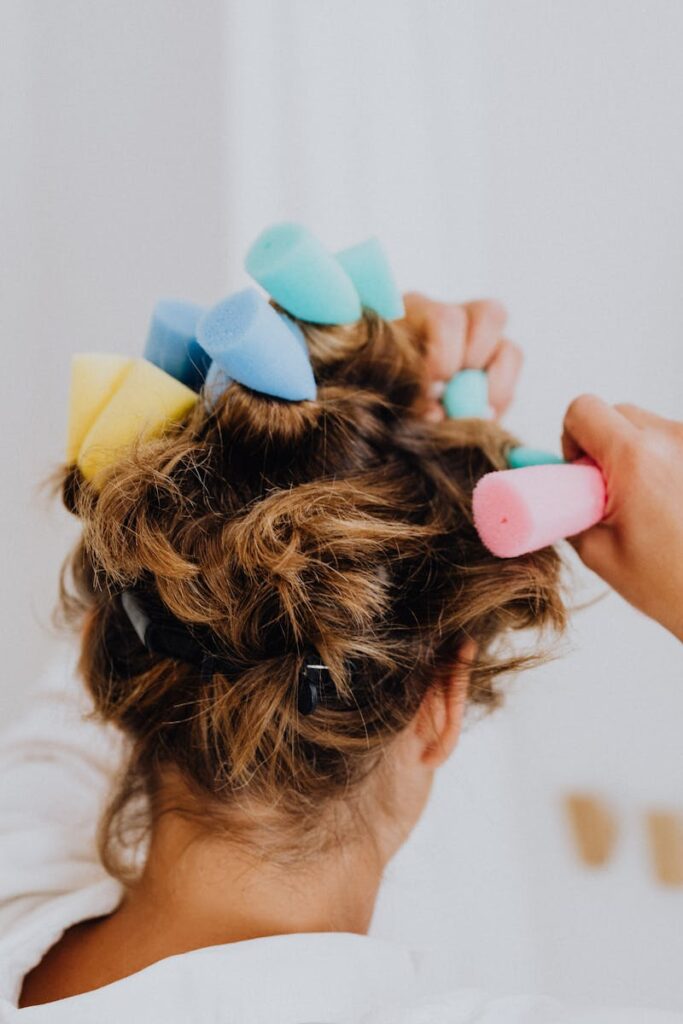Close-up of a woman using colorful foam curlers for hair styling indoors.