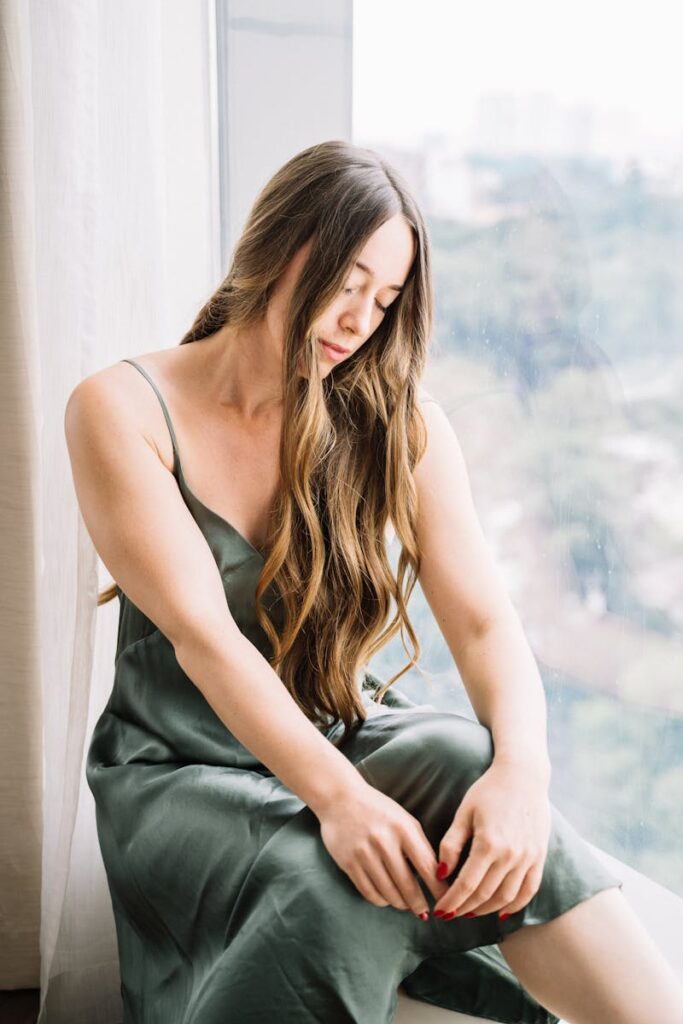 Elegant woman with long hair sitting by a window in natural light.