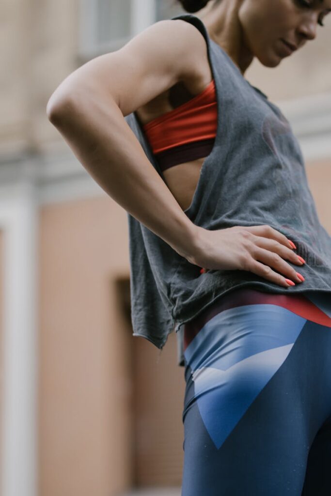 Fit woman wearing athletic leggings and a tank top, posing confidently outdoors.