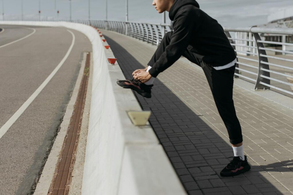 Person in athletic wear stretches on a bridge, preparing for exercise in an urban setting.