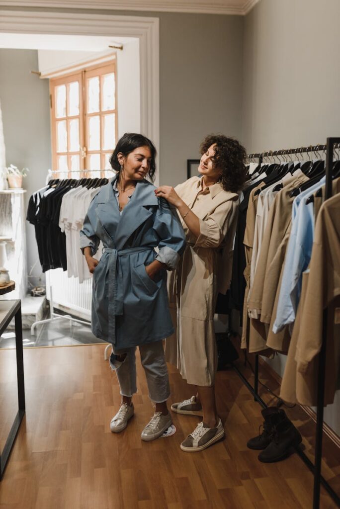 Two women shopping in a boutique, trying on stylish trench coat outfits.