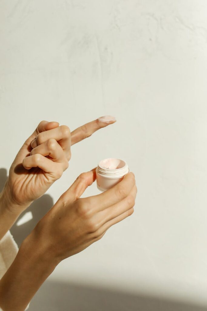 Close-up of hands applying facial cream in soft natural lighting, emphasizing skincare routine.