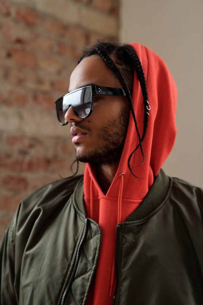 Portrait of a fashionable young man with sunglasses, braids, and a hoodie.
