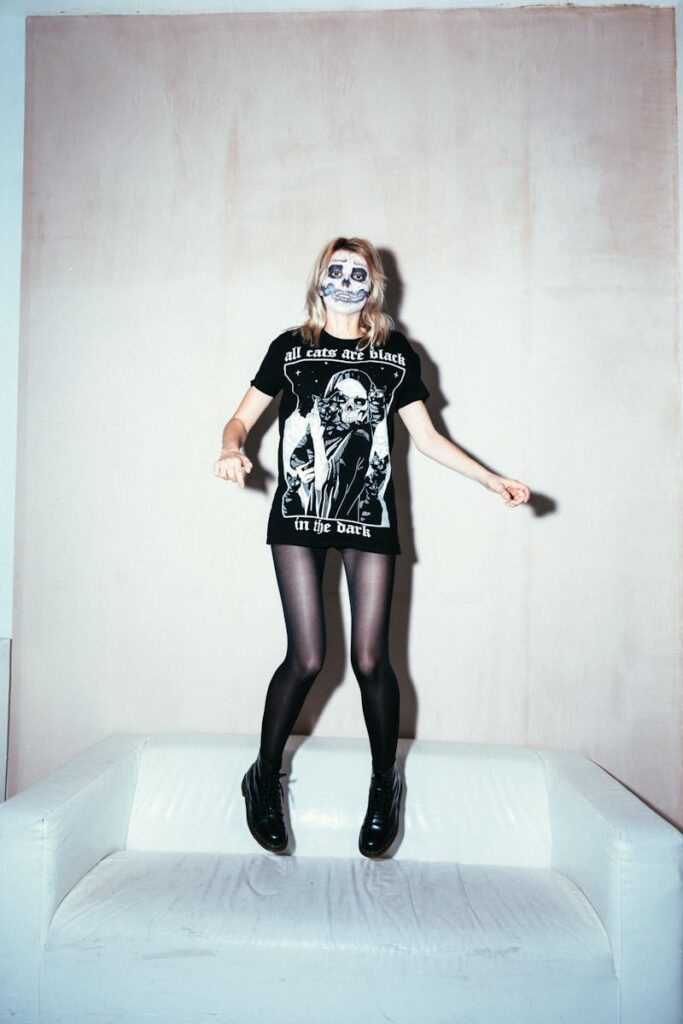 Woman in skull face paint jumping on a sofa, capturing a playful Halloween vibe.