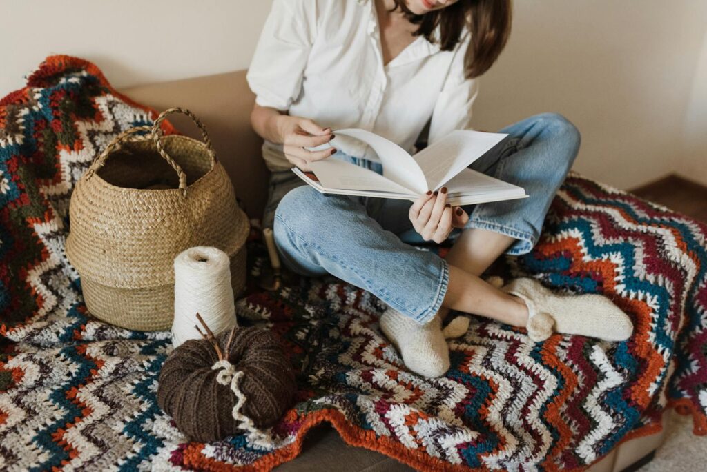 Woman reading on a colorful knit blanket with yarn and basket beside her.