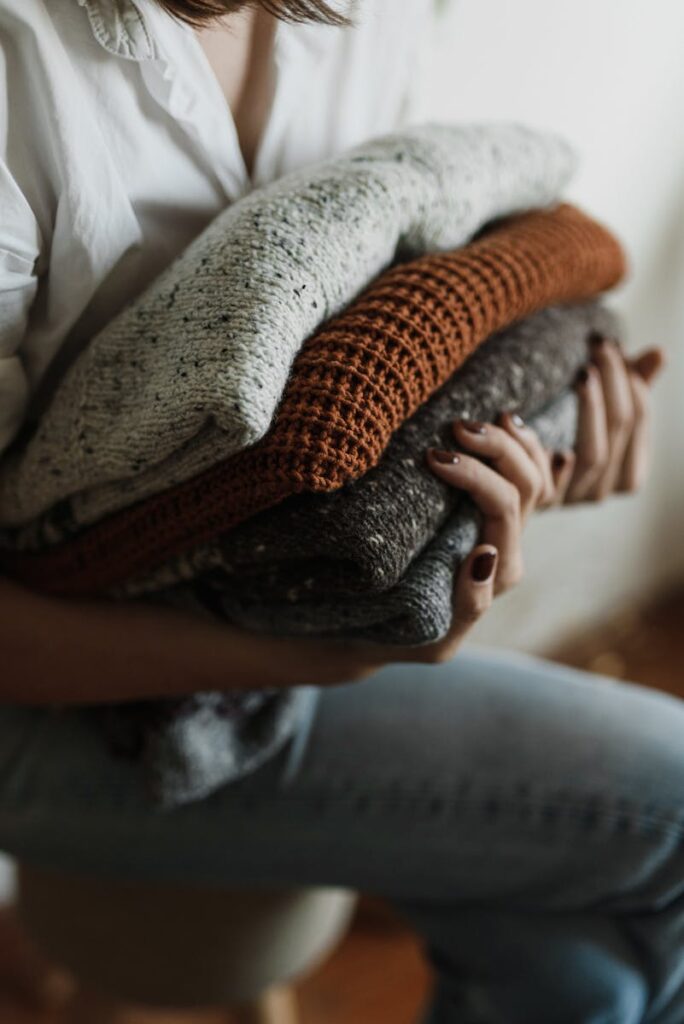 Close-up of a person holding a stack of folded sweaters, evoking warmth and comfort.
