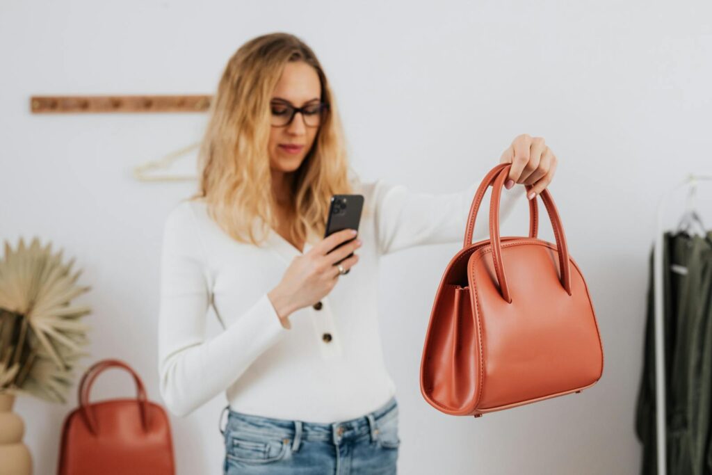 A woman photographs a stylish leather handbag with her smartphone for online selling.