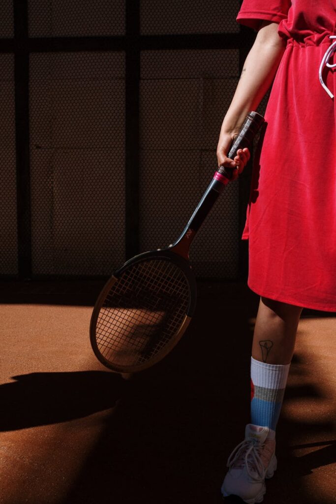 A fashionable tennis player in a red dress holding a racket on a sunlit court.