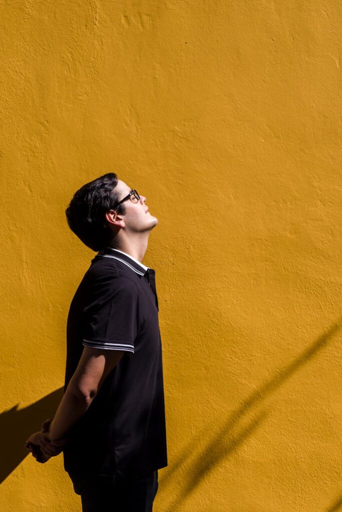 Side view of a man in a black polo shirt standing against a bright yellow wall.